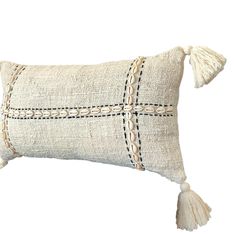 a white pillow with tassels on the edges and a cross stitched design