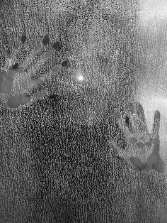 a black and white photo of someone's hand on a window sill with rain drops