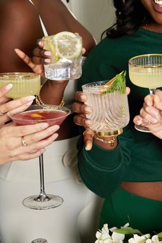 four women are holding up glasses with drinks in them and one woman is wearing a green dress