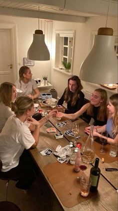 a group of people sitting around a wooden table with wine bottles and cards on it