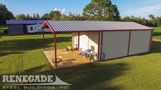 an aerial view of a small metal building in the middle of a grassy field with picnic tables and chairs