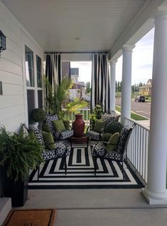 the porch is decorated with black and white striped rugs, green pillows, and potted plants