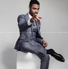 a man in a suit sitting on top of a white box with his hand out