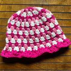 a pink and white crocheted hat sitting on top of a wooden table