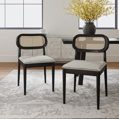 two chairs sitting on top of a rug in front of a vase filled with flowers