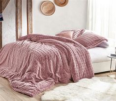 a bed with pink comforter and pillows in a bedroom next to a white rug