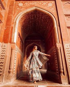 a woman standing in an archway with her arms spread out and wearing a long dress