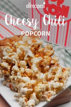 a white plate topped with popcorn next to a red and white striped box filled with cheesy chili popcorn