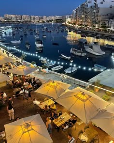 an outdoor dining area with tables and umbrellas next to the water at night time