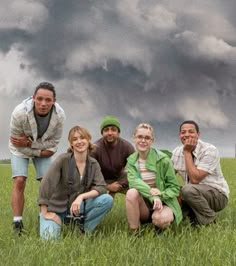 four people are posing for a photo in the grass under a cloudy sky with dark clouds