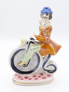 a ceramic figurine of a woman riding a bike with a cat on the back