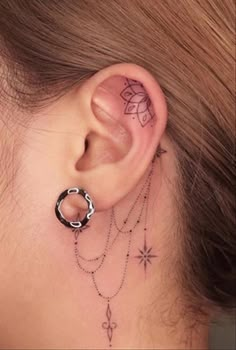 a woman's ear with a chain and flower tattoo on the back of her ear