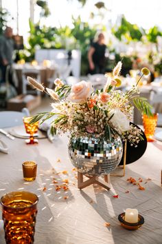 a disco ball centerpiece with flowers and greenery on a table at a party