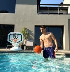 a man standing in the pool with an orange ball near his feet and holding a basketball