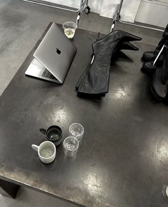 an apple laptop sitting on top of a metal table next to cups and saucers