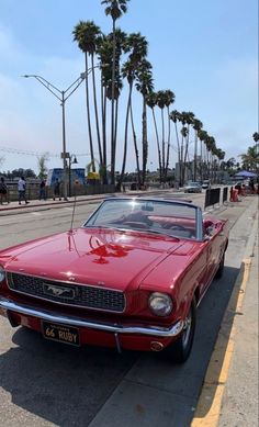 an old red car is parked on the side of the road next to palm trees