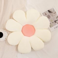 a white flower shaped pillow sitting on top of a bed next to a coffee cup