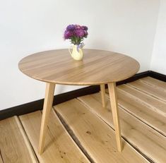 a vase with flowers on top of a wooden table next to a white wall and wood floor