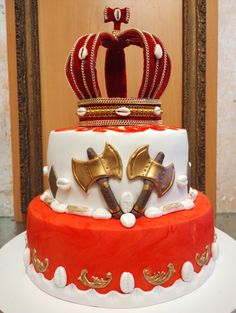 there is a red and white cake with a crown on top that has gold trimmings