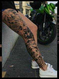 a person with tattoos on their legs sitting next to a motorcycle