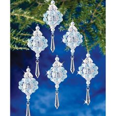 four glass ornaments hanging from a tree branch with snowflakes on it and blue sky in the background