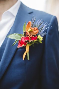 a man wearing a blue suit and red flowers on his boutonniere,