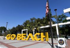 a sign that says go beach next to a flag pole and palm trees in the background