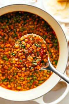 a spoon with some food in it on top of a white bowl filled with soup