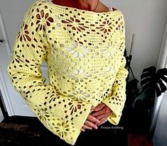 a woman standing in front of a door wearing a yellow crochet sweater and black pants