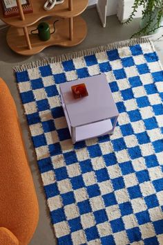 an overhead view of a living room with blue and white checkered rug, orange chair, and coffee table