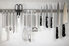 there are many kitchen utensils hanging on the wall with knives and spoons