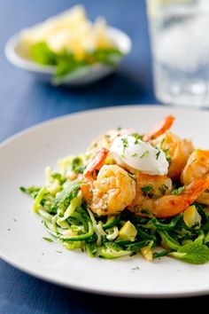 a white plate topped with shrimp and veggies next to a glass of water