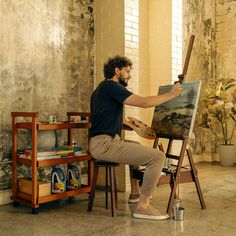 a man sitting in front of an easel painting