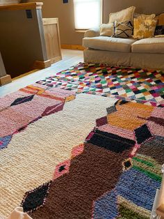 a multicolored rug is on the floor in front of a couch and window