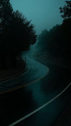 an empty road in the dark with trees on both sides and foggy skies above