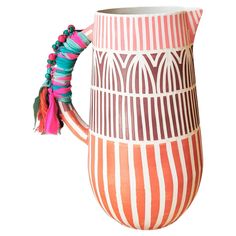 an orange and white striped vase with tassels on the handle is shown against a white background