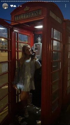 a woman standing in a red phone booth