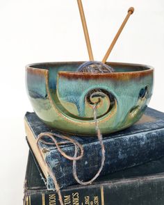 a bowl sitting on top of two books with knitting needles sticking out of the bottom