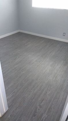 an empty room with gray wood floors and white trim on the walls is seen in this image