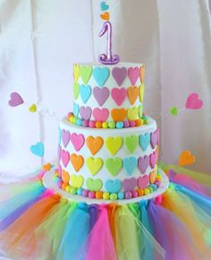 a multi layer cake decorated with hearts and the number one on top is surrounded by colorful tulle