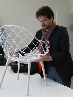 a man standing next to a white chair on top of a table and looking at it