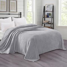 a bed covered in a gray blanket next to two white pillows on top of a wooden floor