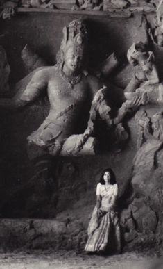 an old black and white photo of a woman standing in front of a stone statue