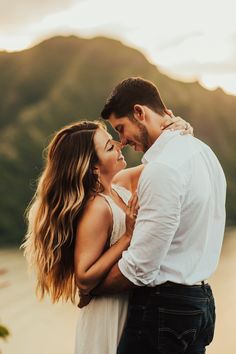 a man and woman standing next to each other in front of the ocean at sunset