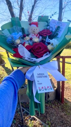 a person holding a bouquet of flowers with a teddy bear on it in front of some trees