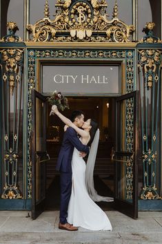 a bride and groom kissing in front of the city hall entrance to their wedding ceremony