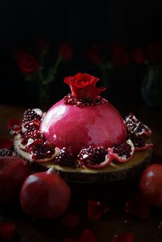 a pomegranate covered in red flowers and blackberries on a wooden table