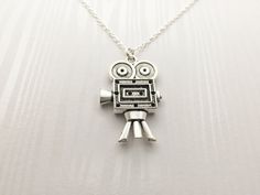 a silver robot necklace on a white surface with the eyes open and one eye closed