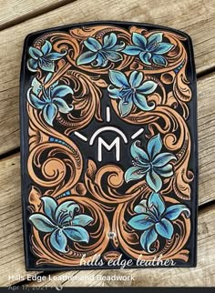 an intricately designed leather case with blue flowers on it and the letter m in the center