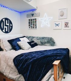 a bedroom with white walls and blue blankets on the bedspread is lit up by neon lights